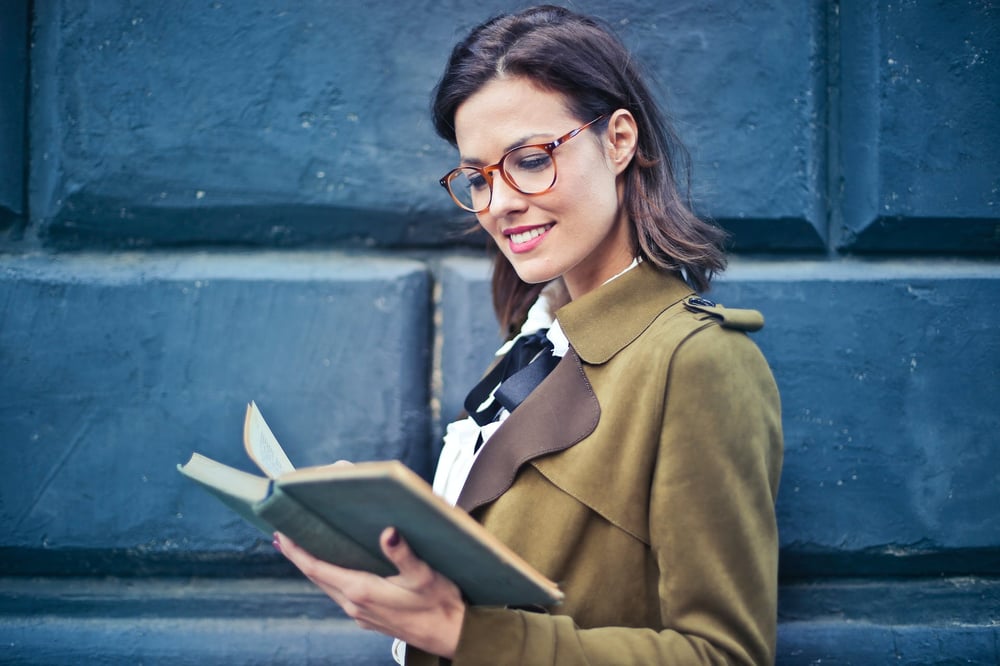 A smiling person in glasses reads a book.