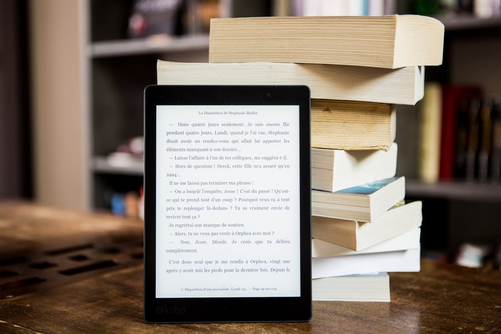 An e-reader propped up against a stack of books.