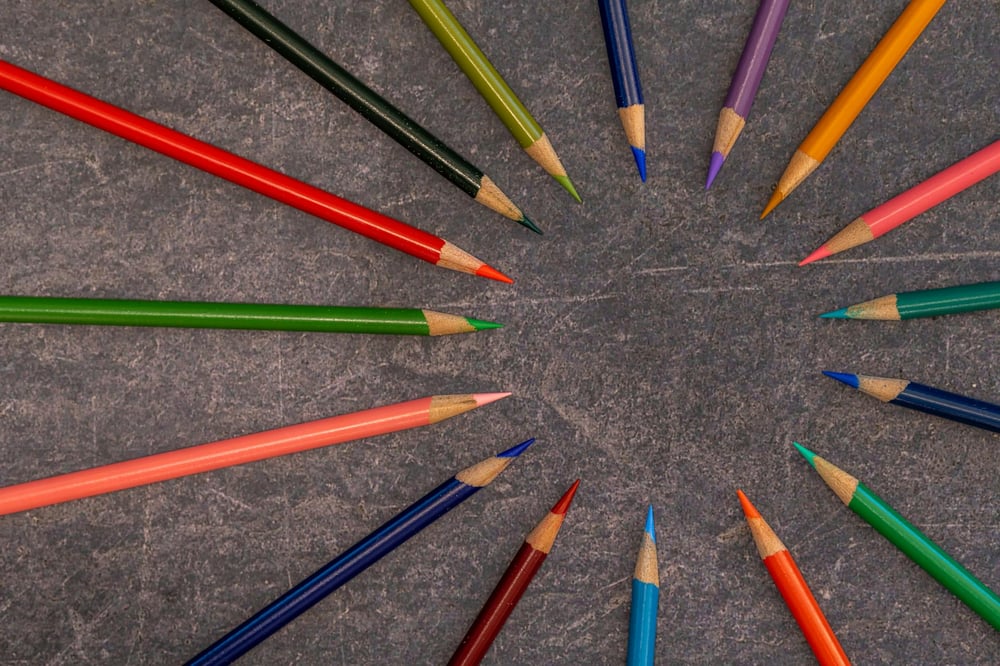 Colored pencils arranged in a circle on a dark background with their points in the middle.