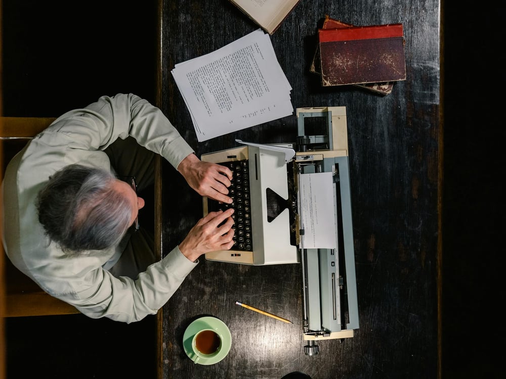 Overhead view of a writer typing a manuscript on a vintage typewriter.