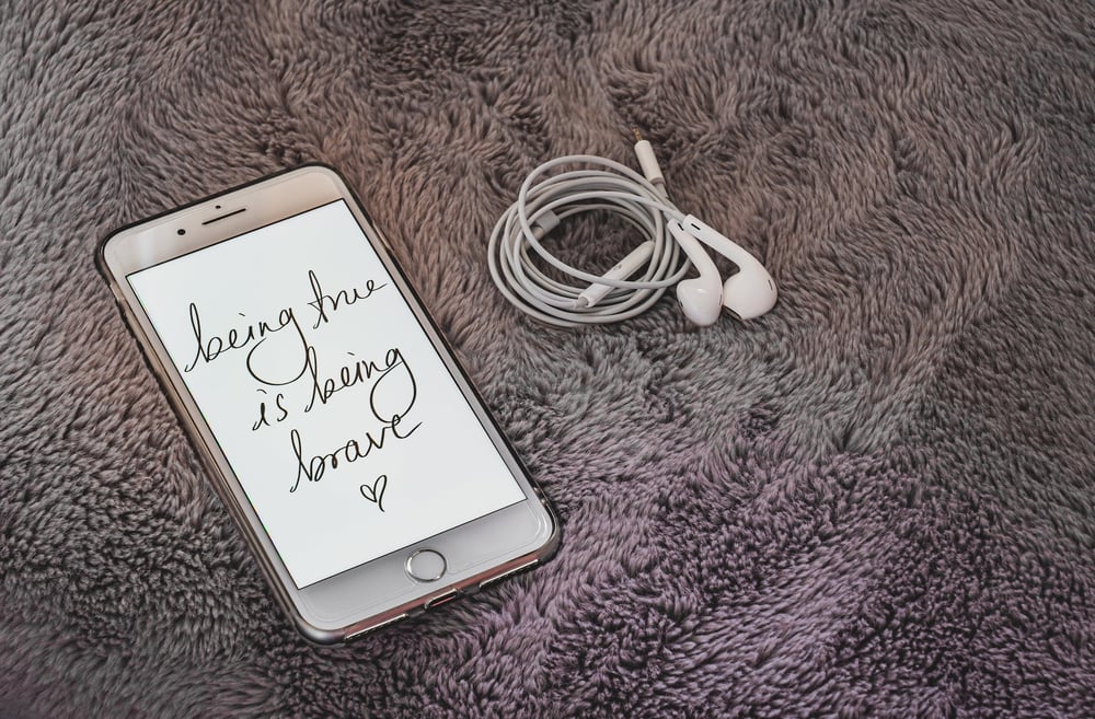 Wound up ear buds on a carpet beside a white phone with a screen reading: