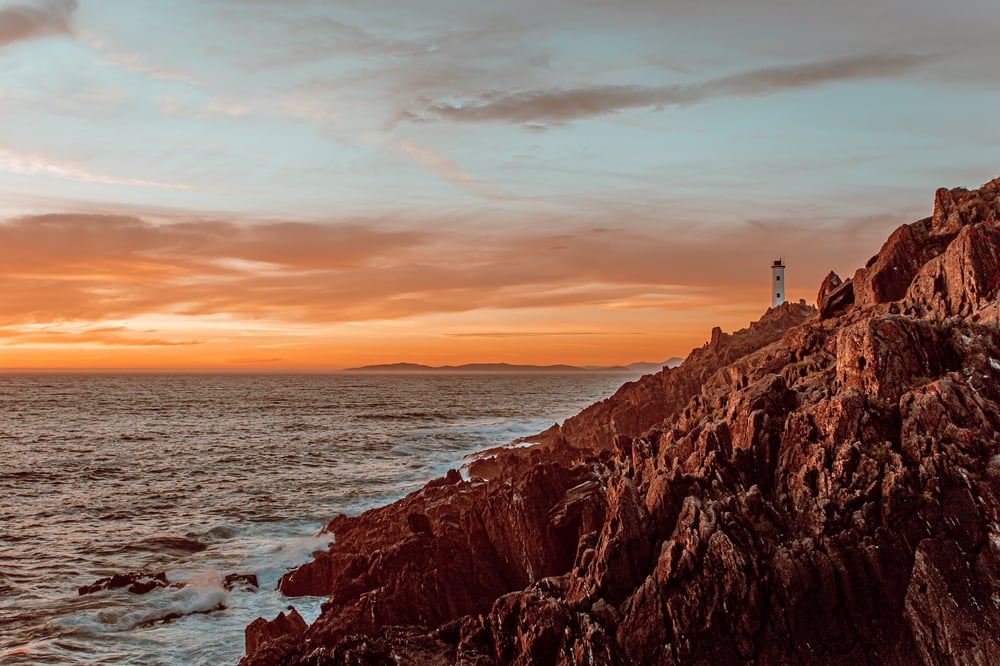 A lighthouse on a rugged coast at sunset.