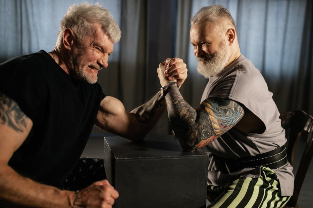 Two older people arm wrestling.