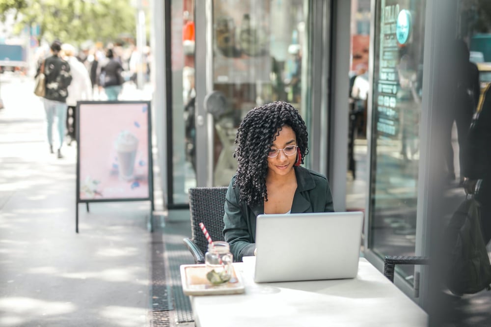 A person works on a laptop at a table on the sidewalk outside of a café.