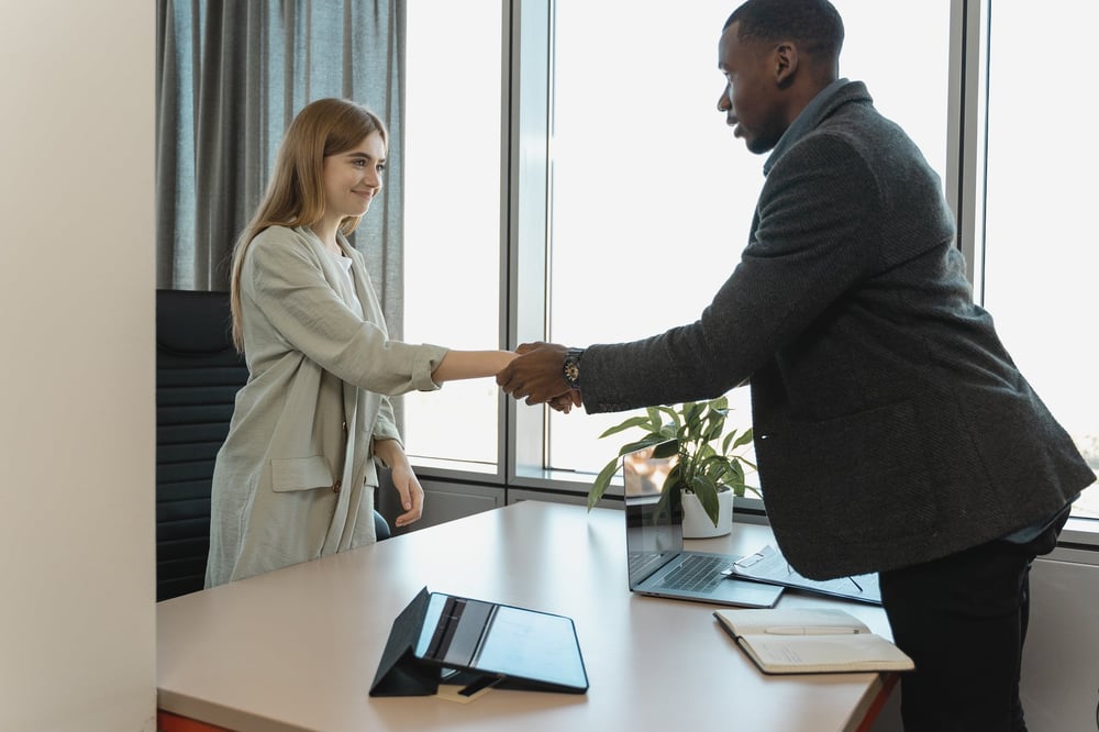 Two people shake hands over a desk after a job interview.