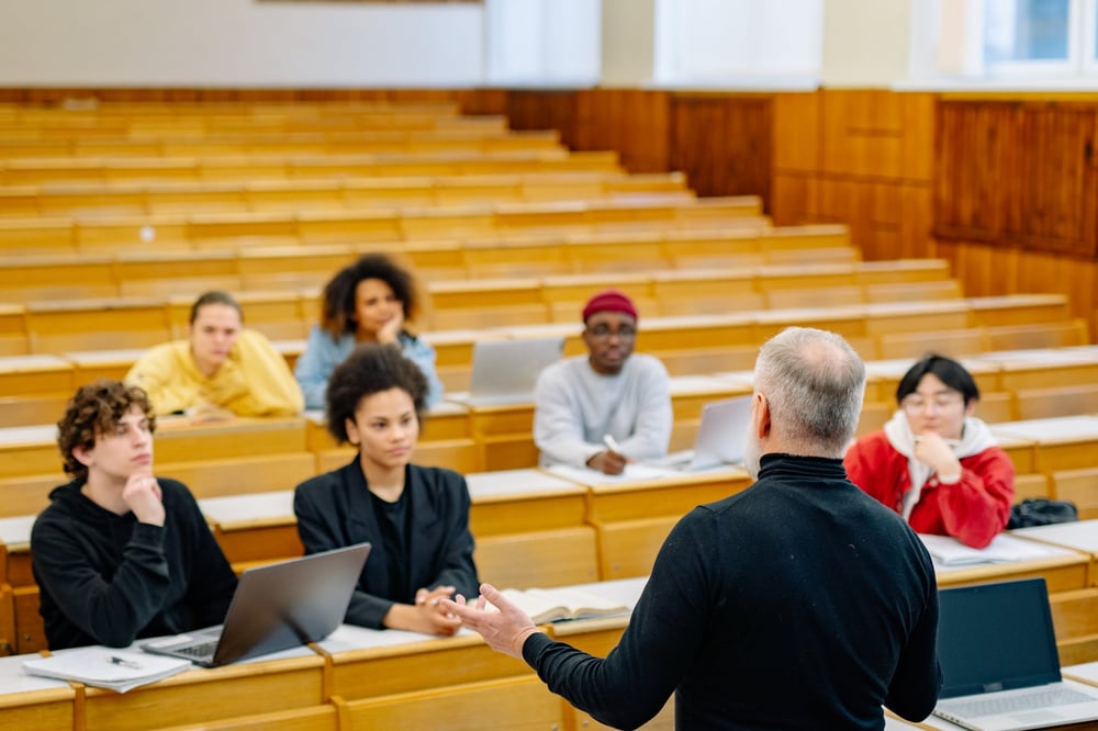 A professor stands at the front of an auditorium, lecturing creative writing students.