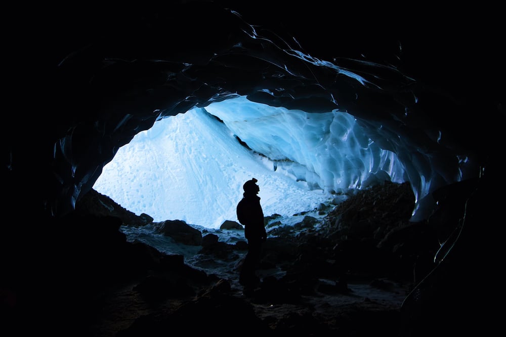 A sillouette of a person standing in the eye-shaped opening of an icy cave.
