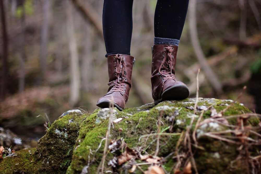 Feat wearing tall hiking boots stand on a mossy rock in nature.