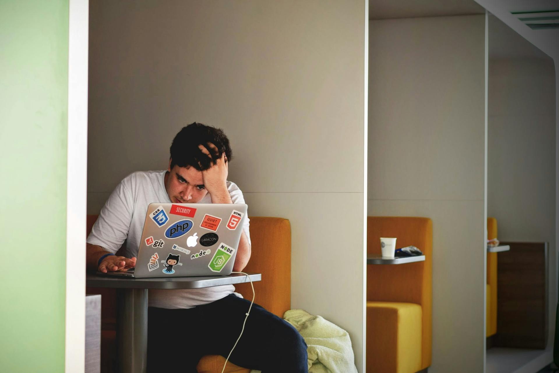 A stressed-looking person runs a hand through their hair as they look at their computer in a booth.