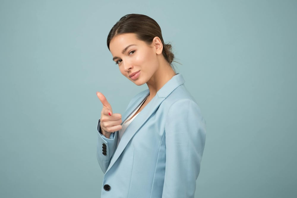 A confident person in a blue blazer shoots a finger gun at the camera.