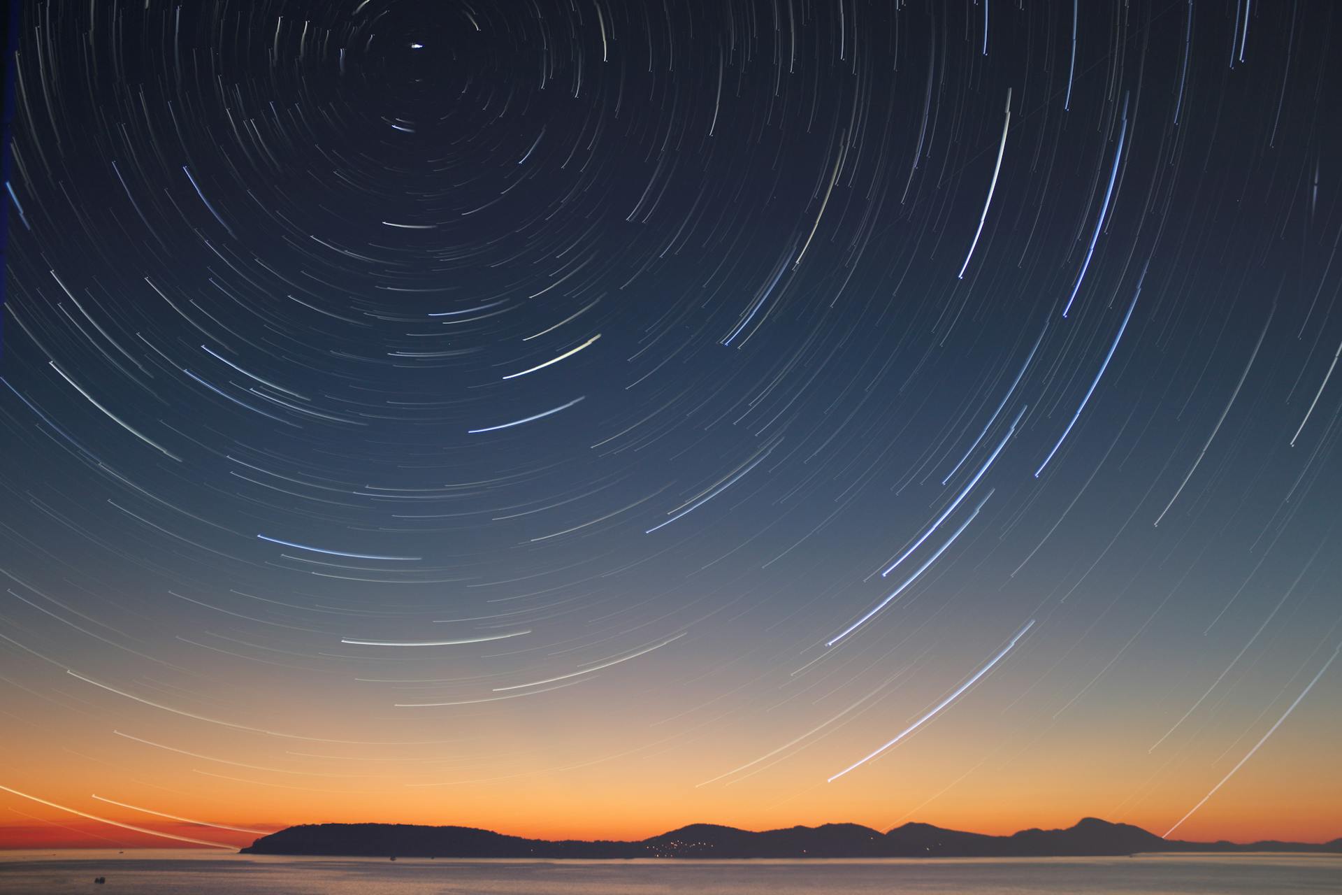 A hilly landscape at sunrise with circular streaks in the sky showing the path of stars.