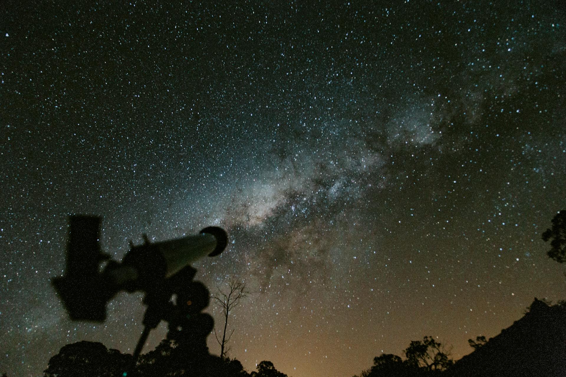 A telescope points up toward the Milky Way in the night sky.