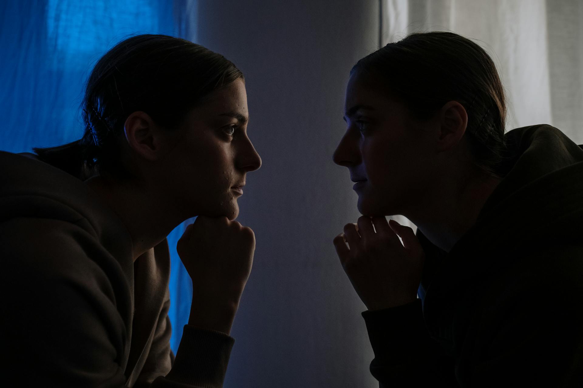 Two identical looking people stare at each other in the dark.