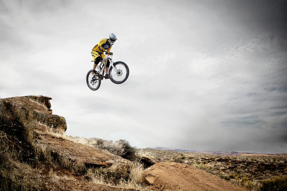 A person jumps off a large rock formation on a bike.