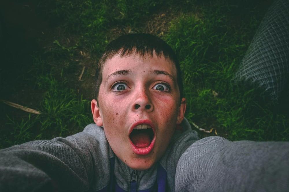 A child with a wide open mouth reaches out in shock.