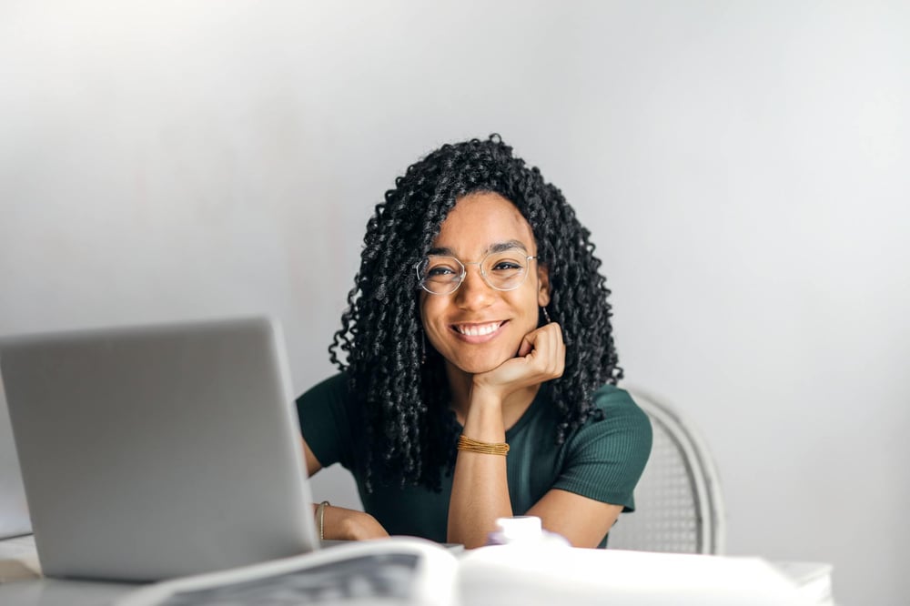 A person in glasses smiles from behind a laptop.