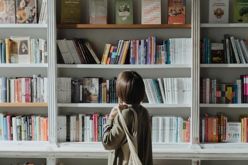 A person with a bob haircut peruses the white shelves of a bookstore.