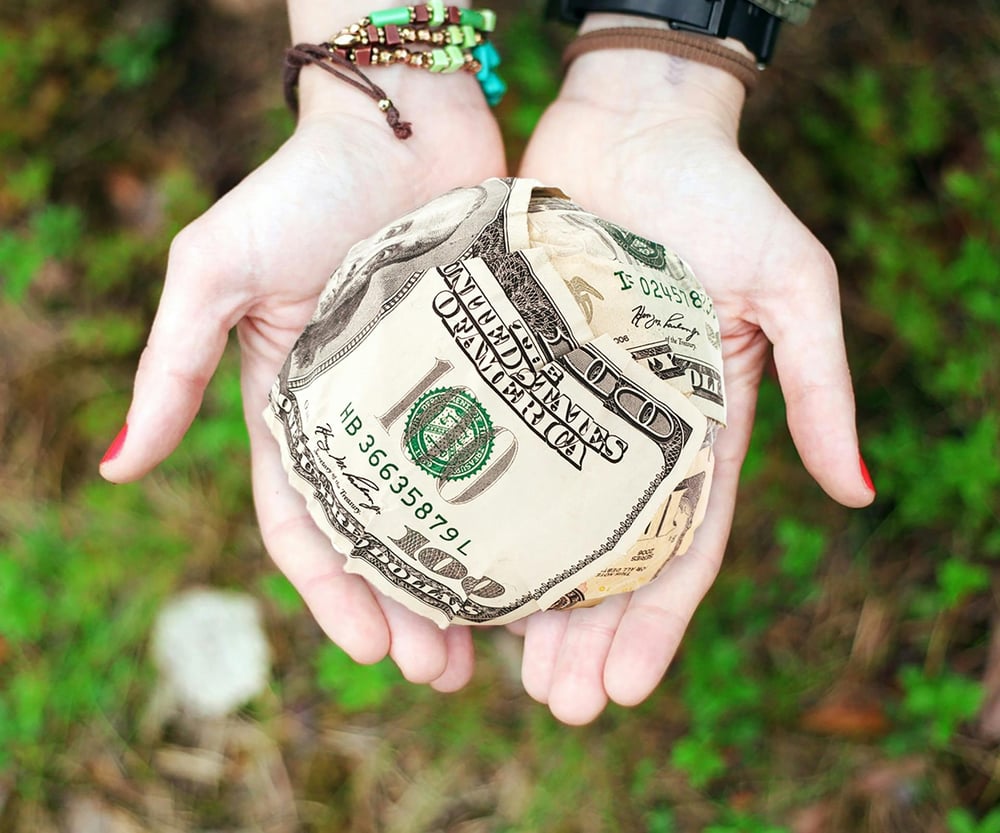 A pair of hands hold a perfect ball made of $100 bills.