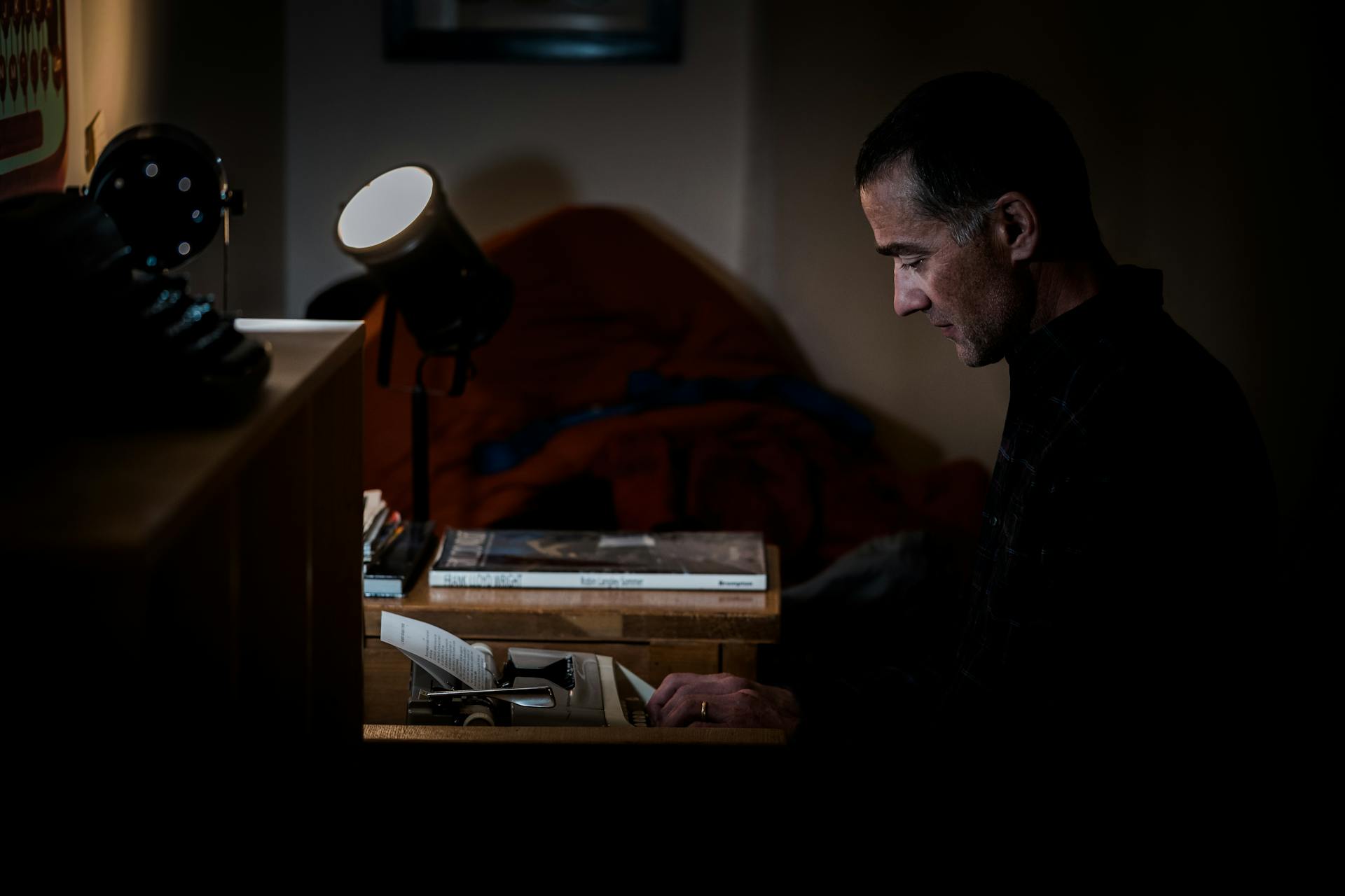 A writer types on a vintage typewriter at a desk in a dark room.