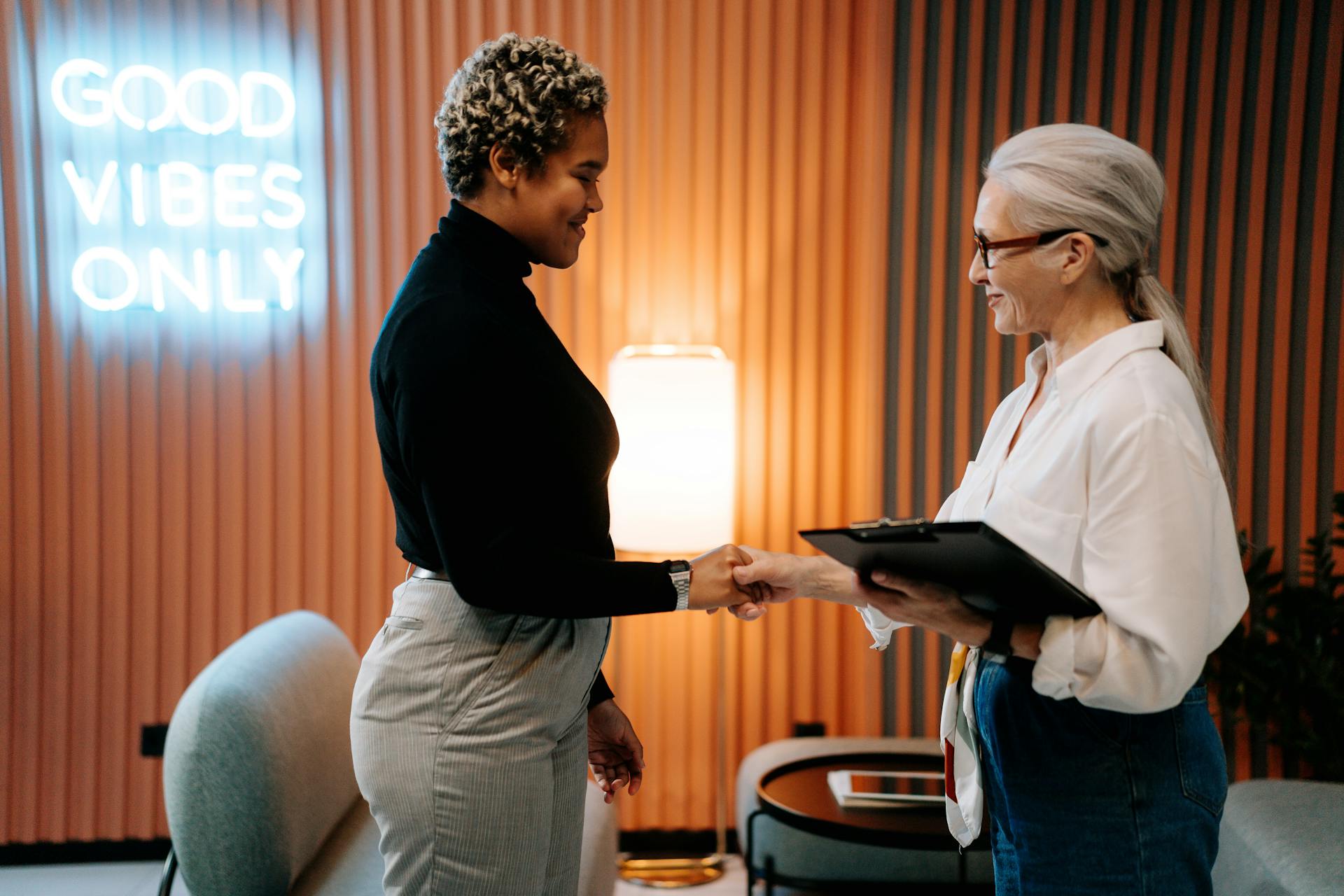 Two professionally dressed people shake hands in a modern office.