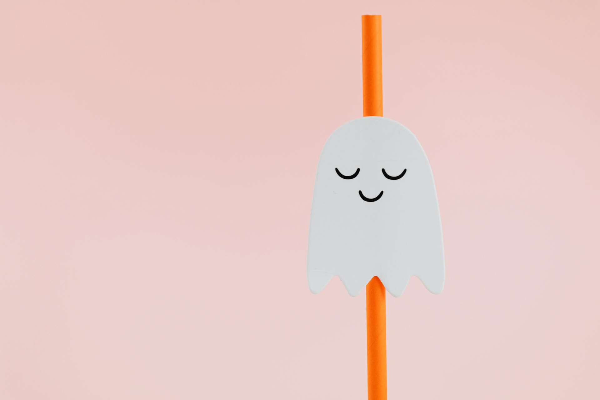 A little ghost decoration on an orange straw.
