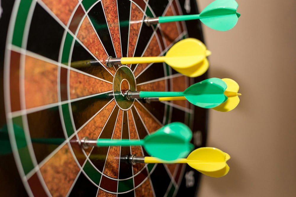 Several yellow and green darts stuck in a dart board.