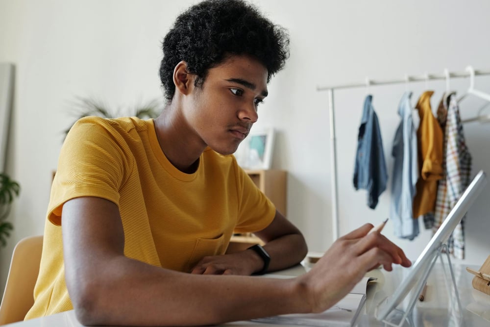 A person touches the screen of a tablet propped up on a desk.
