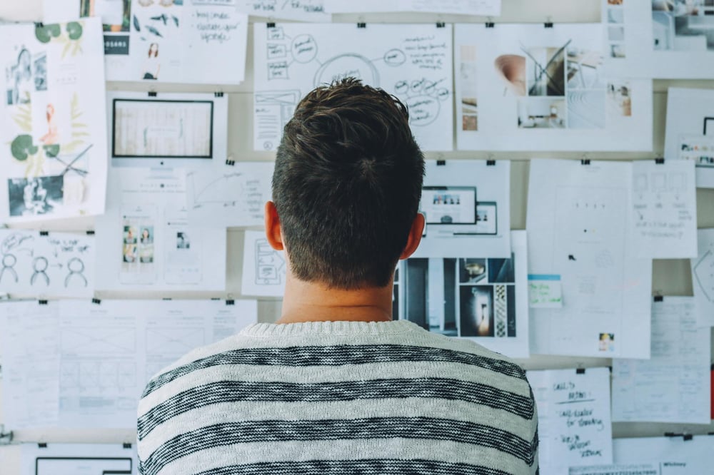 A person stars at a large corkboard full of notes and images.