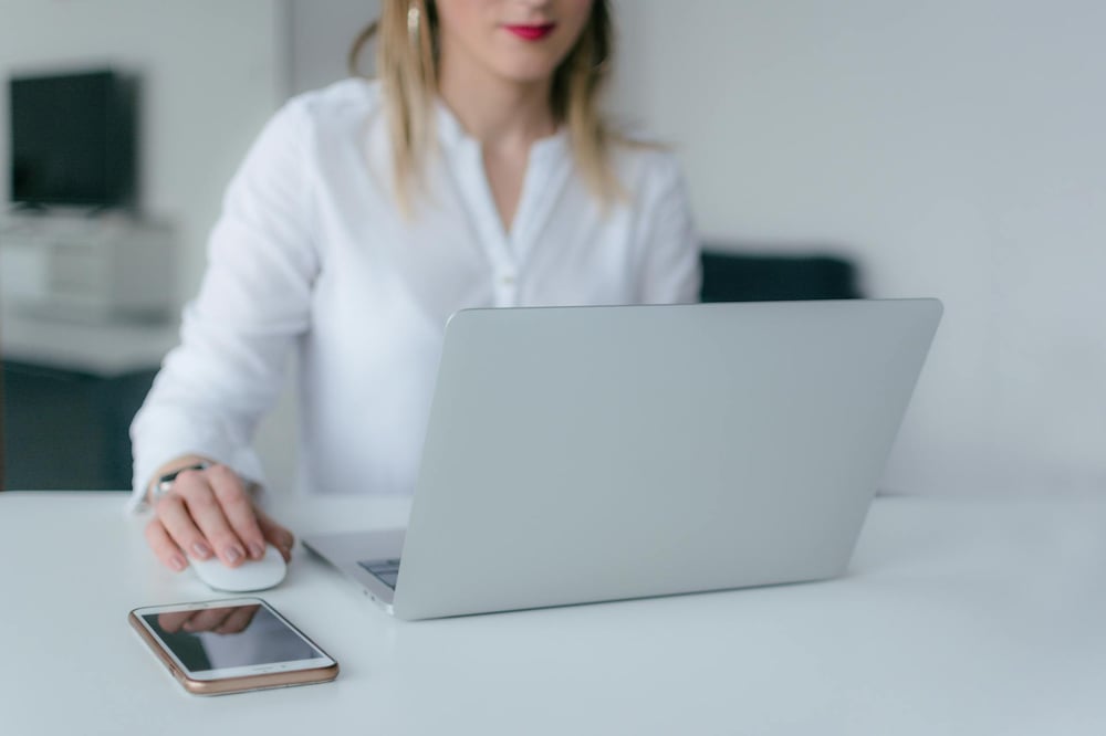 A person in a white blouse sits at a desk typing on a laptop.