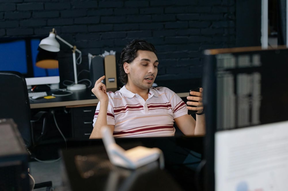 A person sitting at a desk, reading something off their phone.