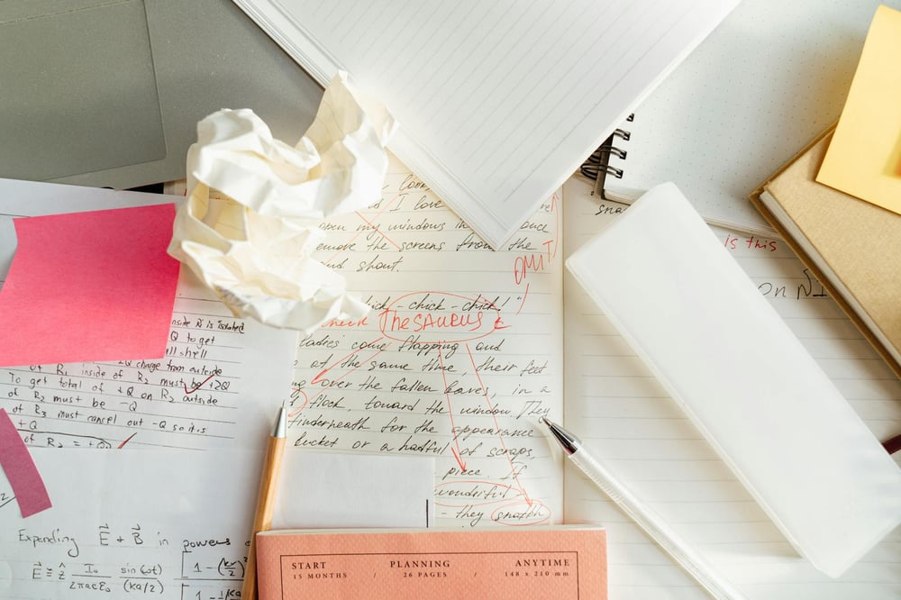 A pile of papers and notebooks with pages that have been copy edited in red pen.