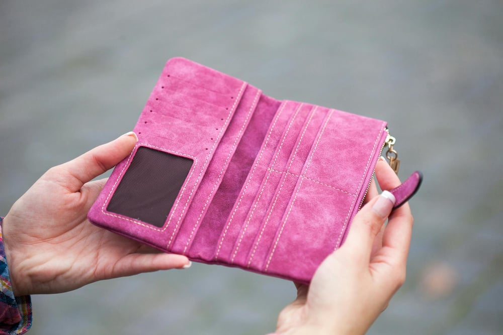 Hands open an empty pink wallet.