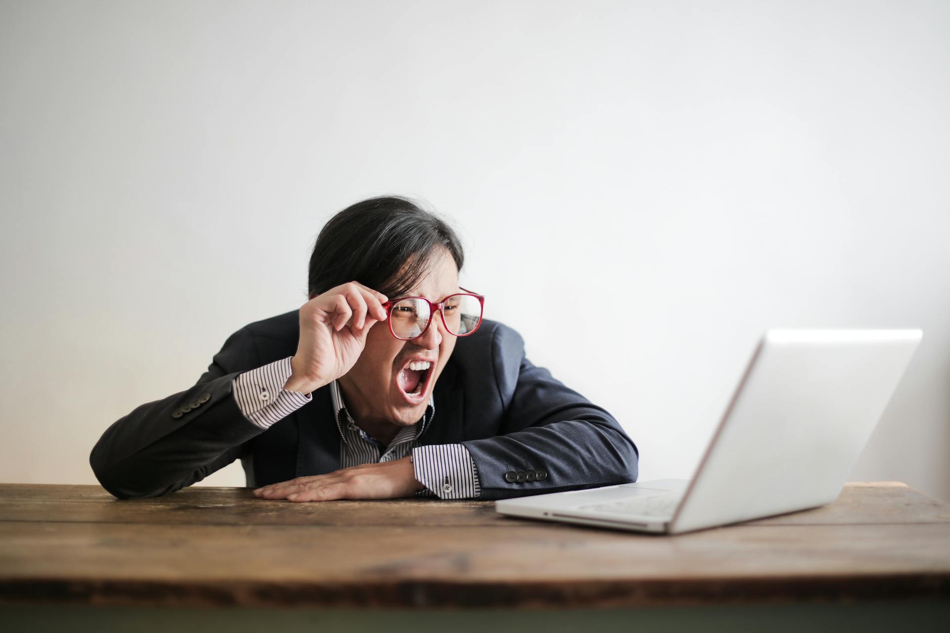 A person holds red-framed glasses on their face and looks at a computer screen with a shocked expression.