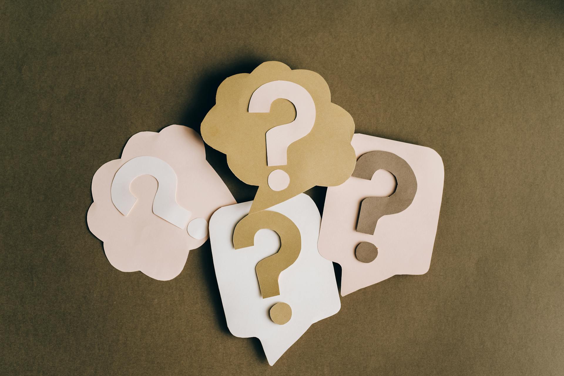 A cluster of four brown and pink paper question marks on top of a brown background.