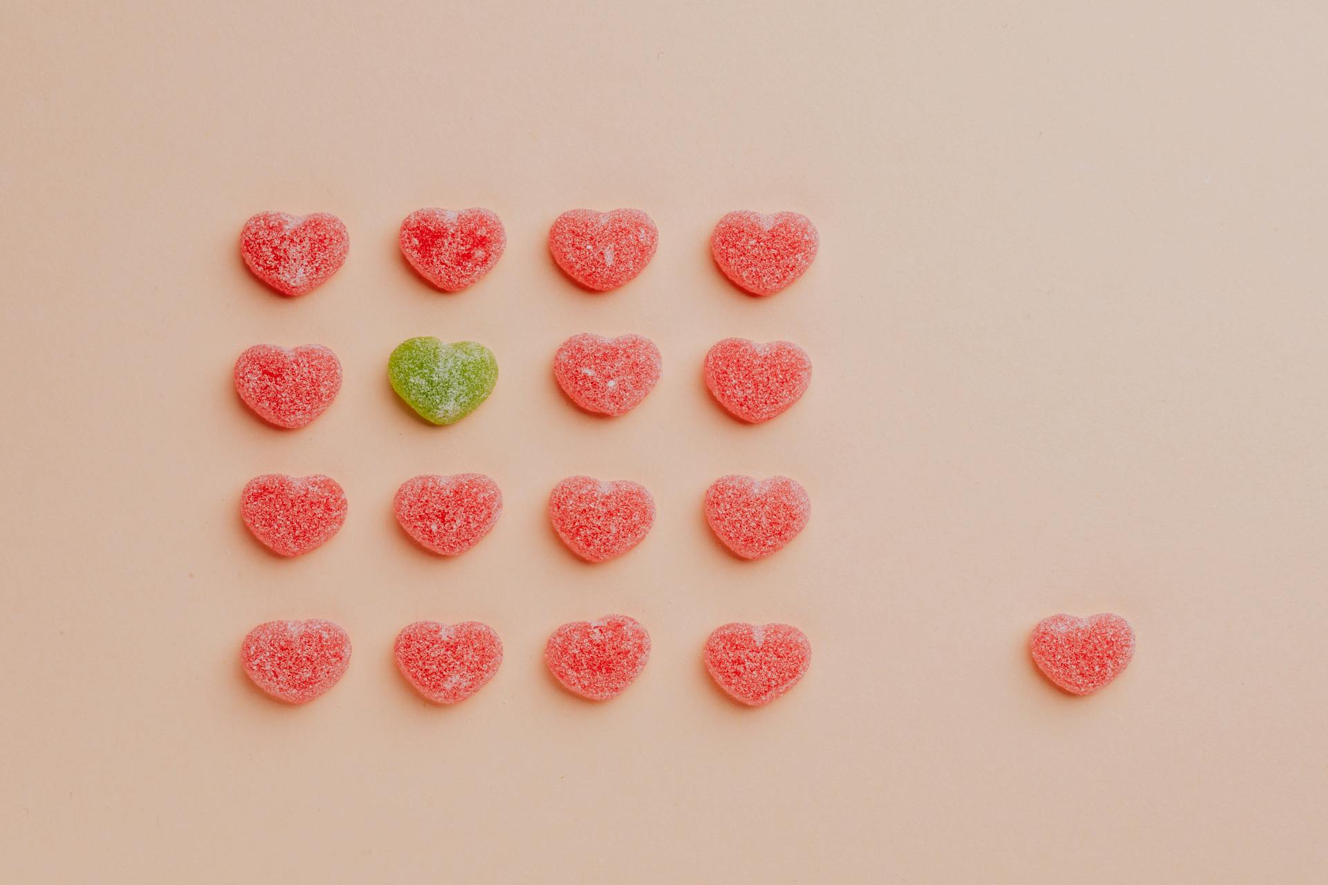 Several red candy hearts with one green candy heart in the middle.
