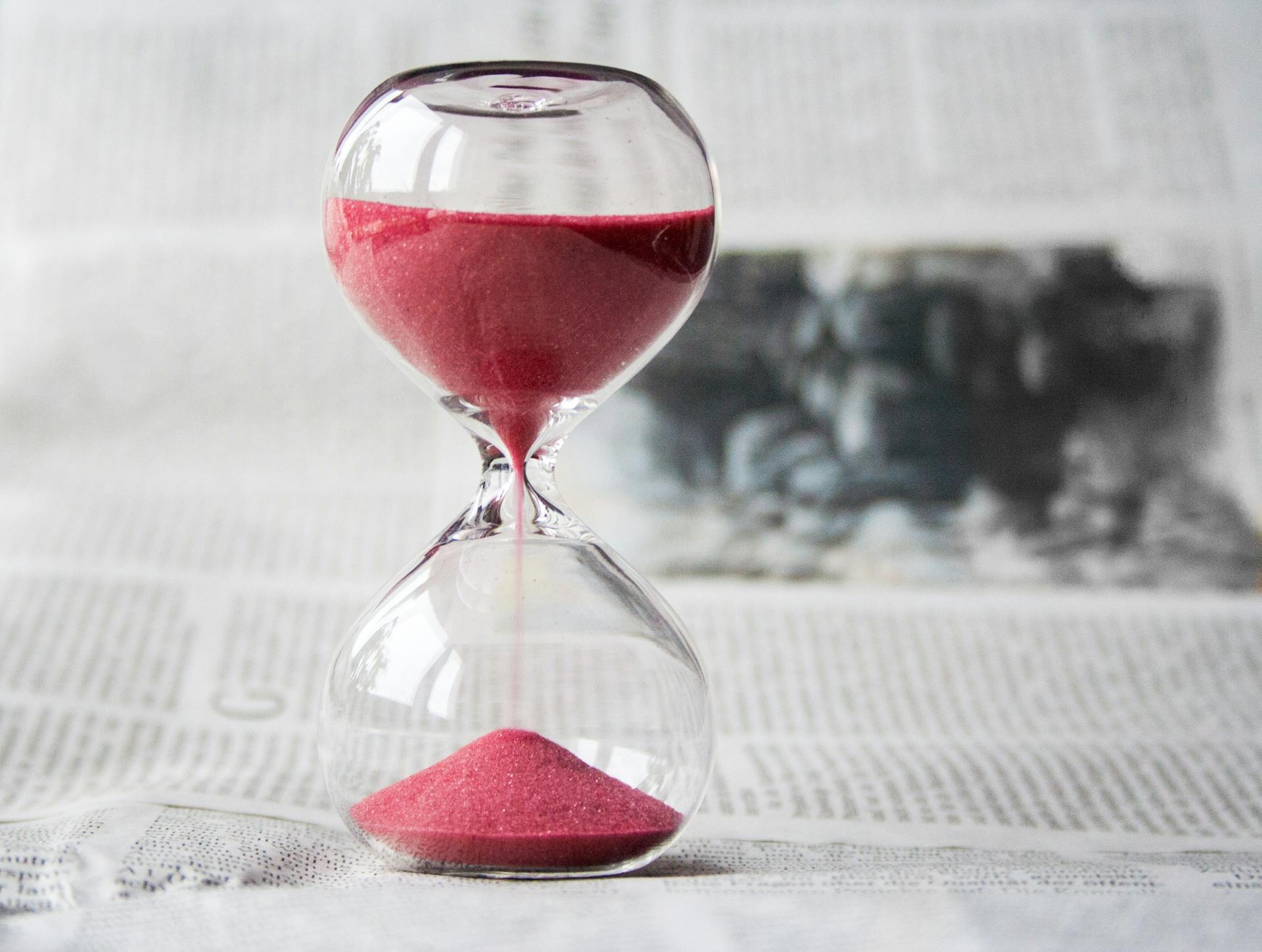 An hourglass with red sand sits on top of a newspaper.