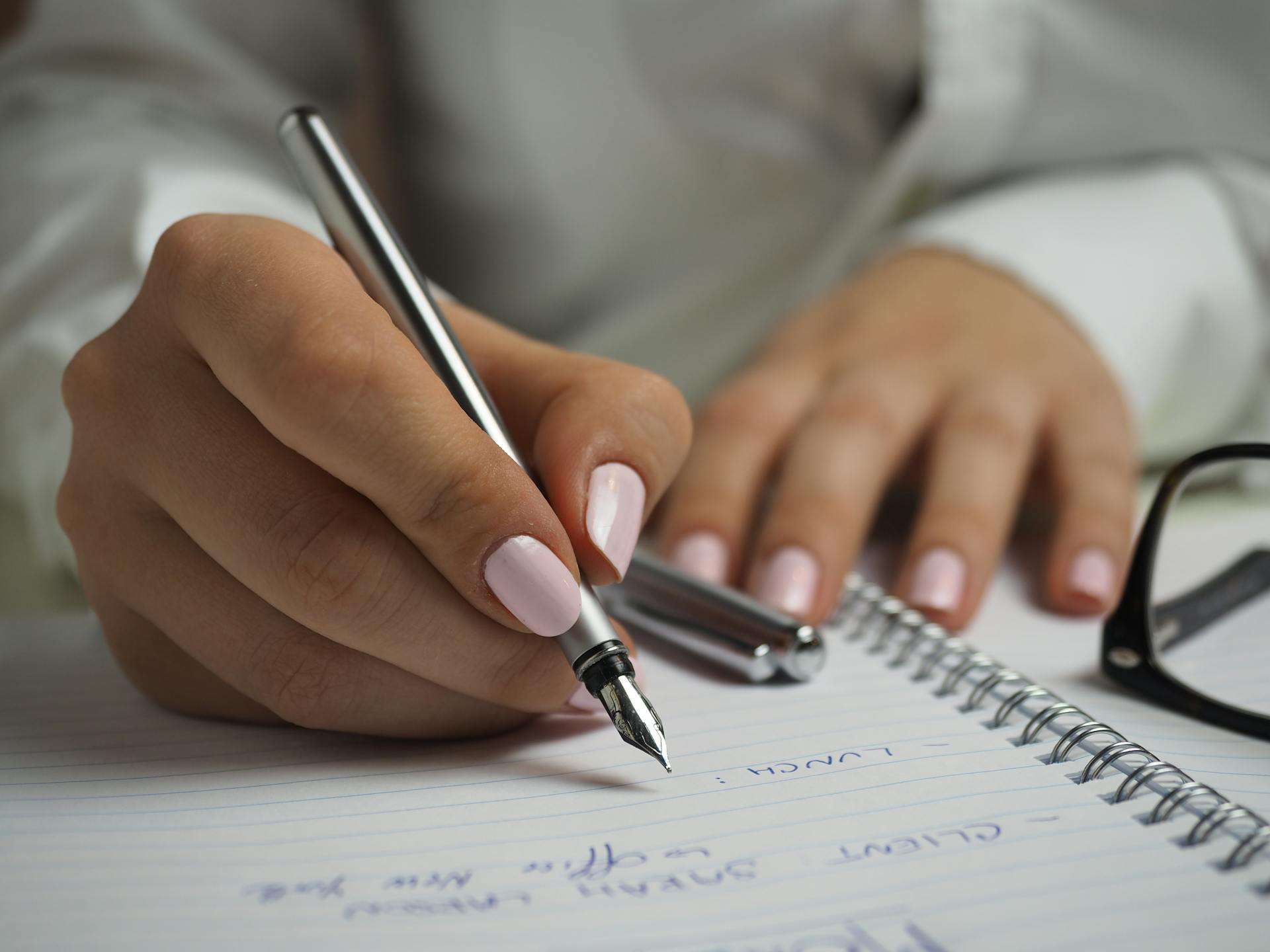 Hands with pink fingernails write in a notebook.