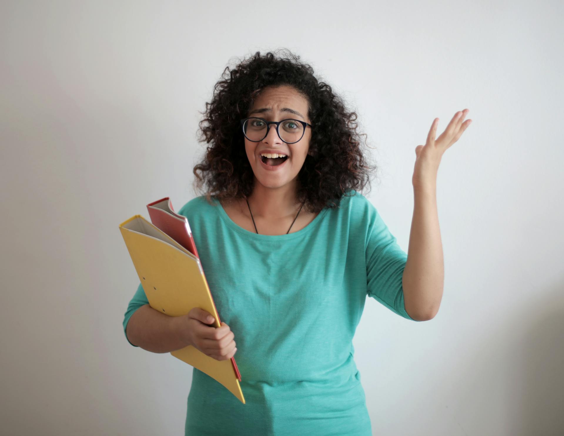 A person holding binders smiles and gestures with their free hand.