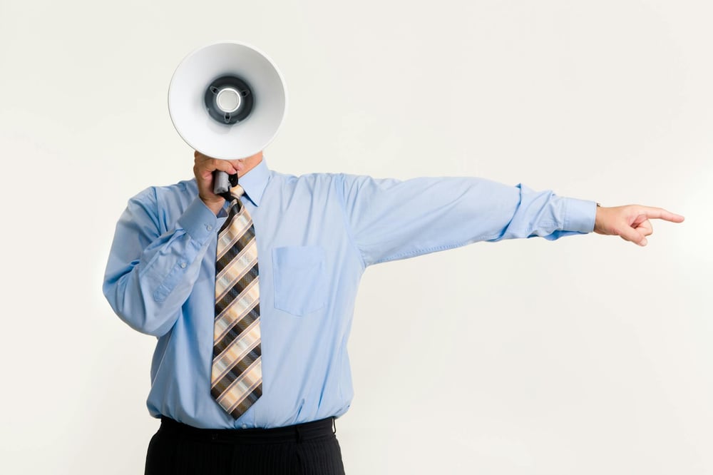 A person in a shirt and tie holds a bullhorn in front of their face and points off to the side.