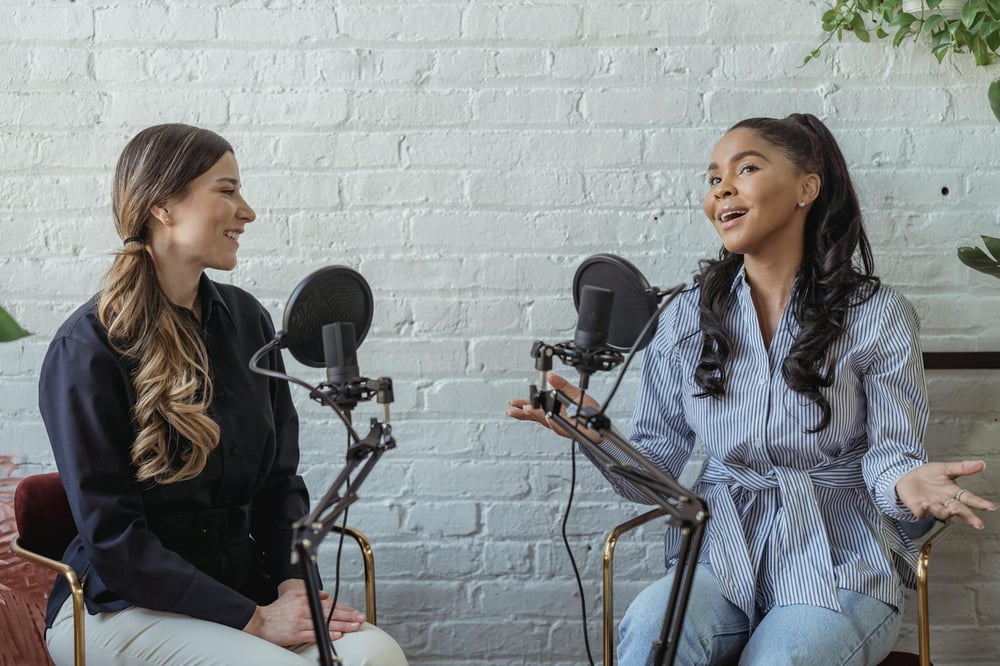 Two smiling people have a conversation into microphones.