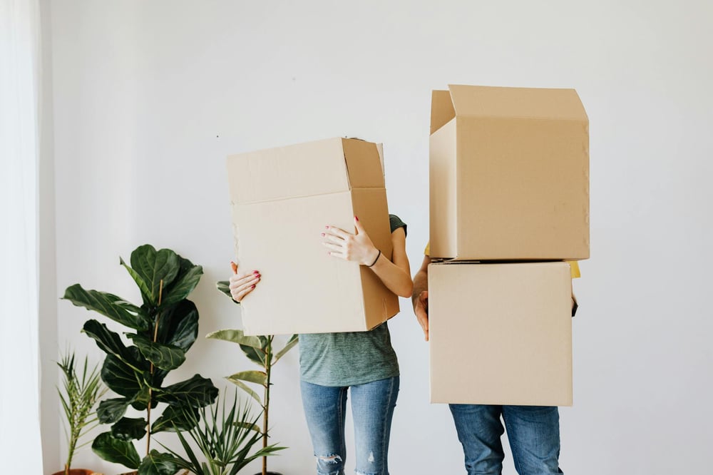 Two people carry big boxes that block their faces.