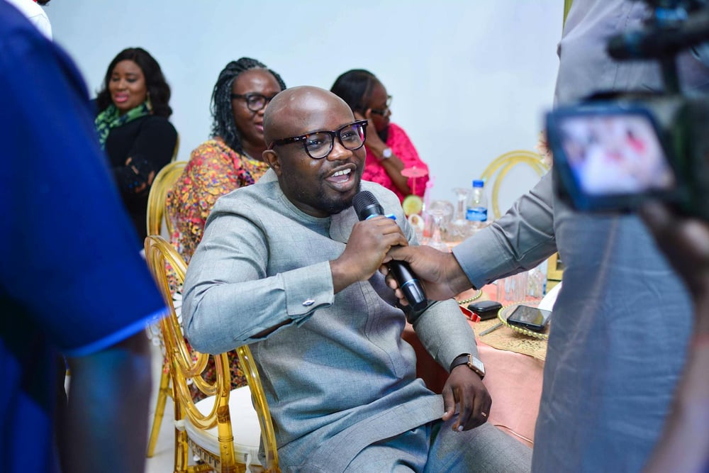 A person sitting at a table at an event speaks into a microphone.
