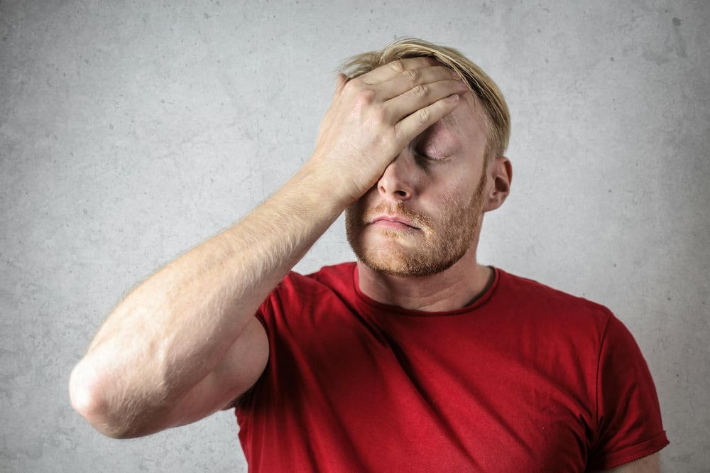 A person in a red shirt looks stressed and touches a hand to their forehead.