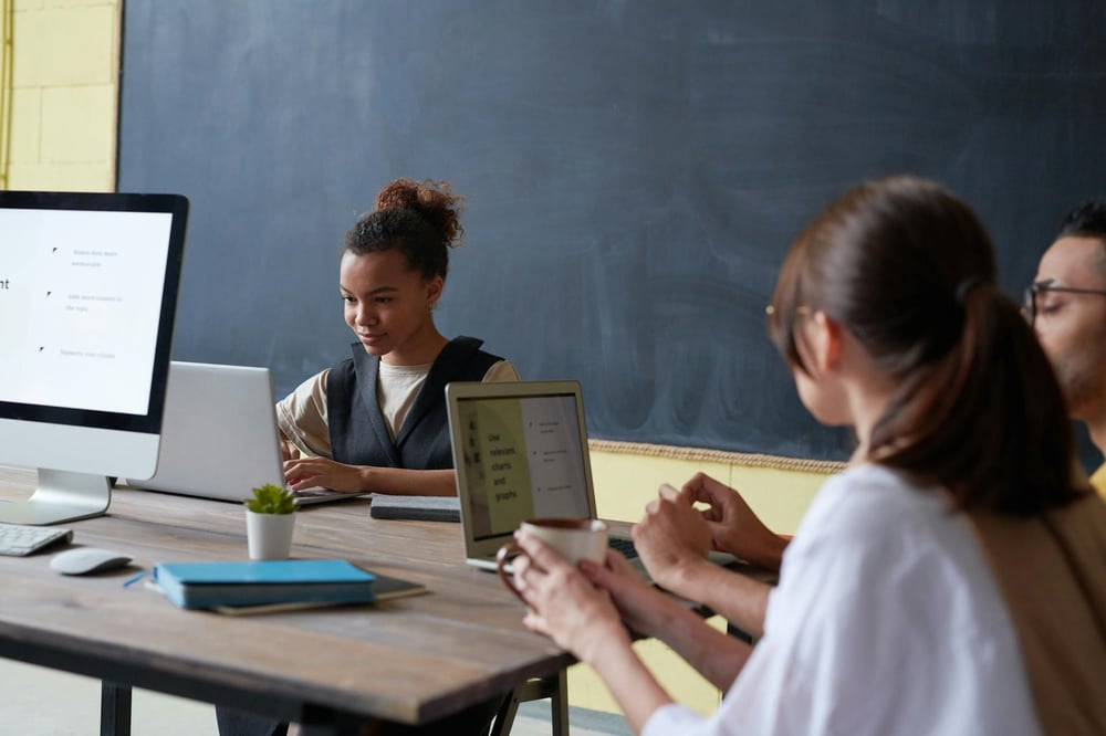 Students sit together at a large table, typing on computers.