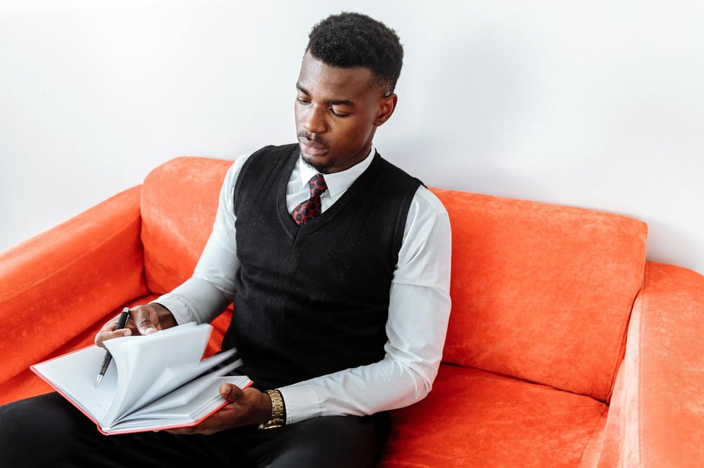 A person sits on an oversized orange chair and flips through a notebook.