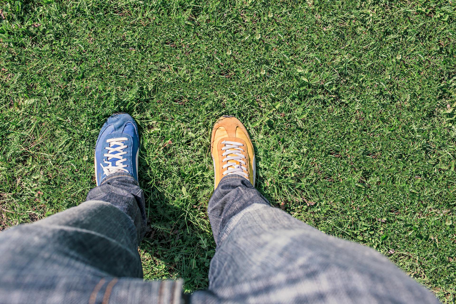 Overhead view of two feet standing in the grass, one wearing a blue shoe and the other wearing a yellow shoe.