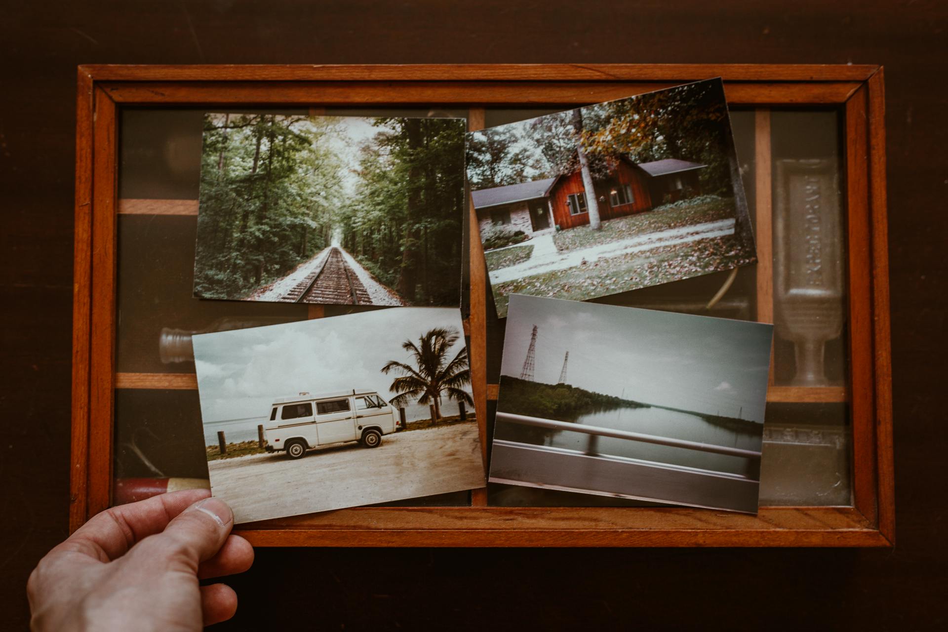 A hand holds a photo of a vintage van up to an antique display box alongside three other travel-themed pictures.