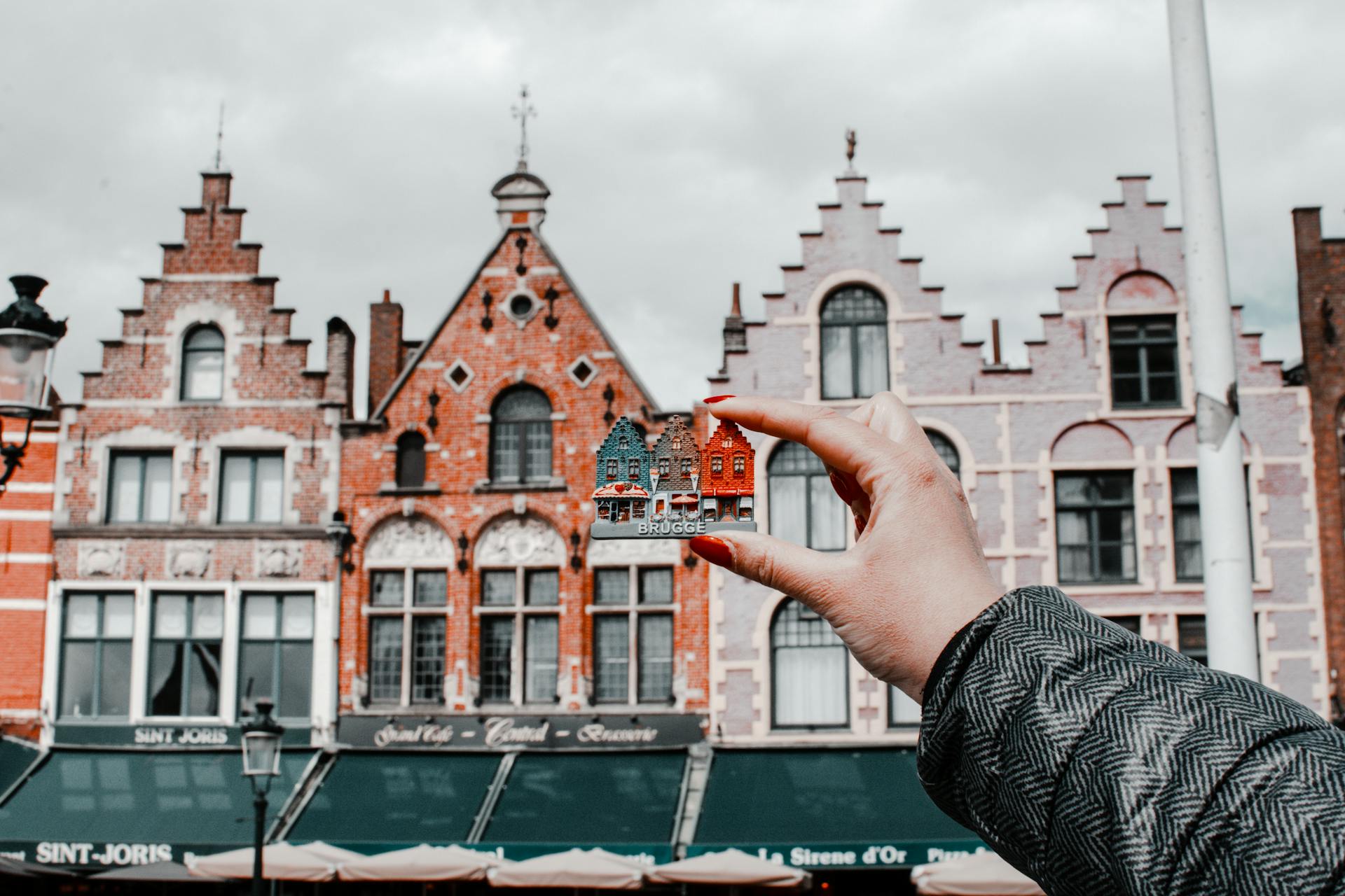 A hand holds a magnet depicting a row of buildings up in front of the actual buildings the image is based on.