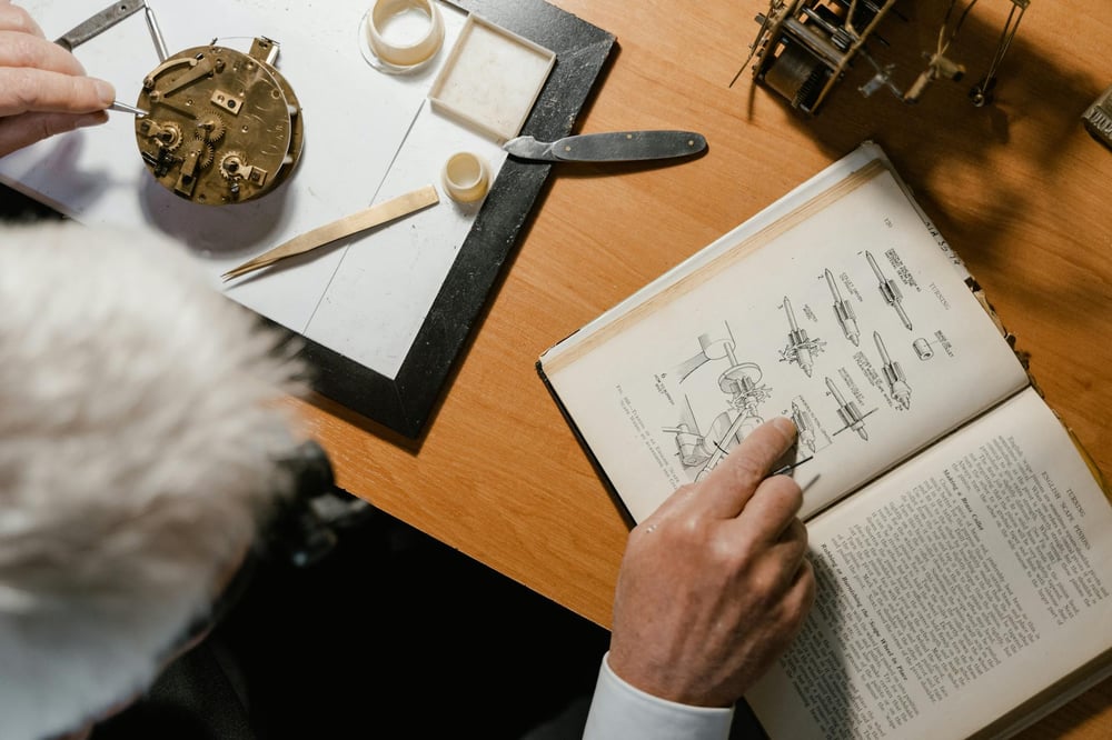 Overhead view of a person consulting an illustrated guide for repairing a metal gadget that sits on the table in front of them.