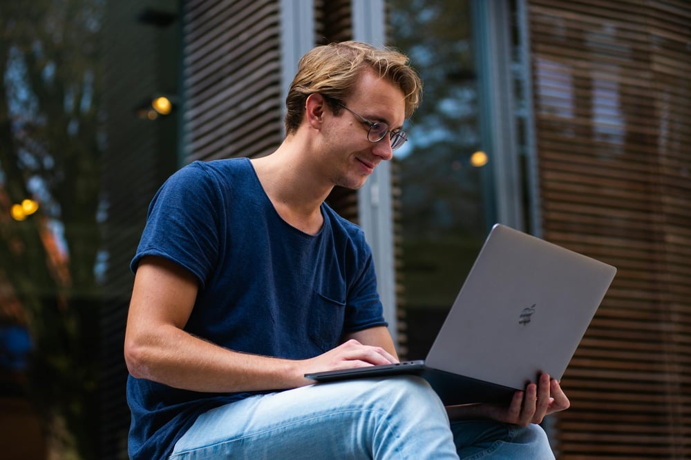 A person sitting outside, writing on a laptop.